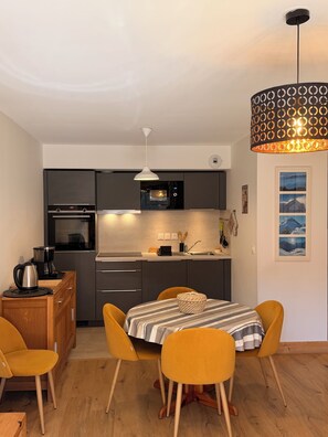 Una cocina compacta con electrodomésticos modernos, una mesa de comedor con sillas y una lámpara con un diseño original.