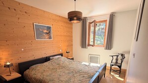 Ein Schlafzimmer mit Holzwand, einem Bett, einem Nachttisch mit Lampe, einem Sessel und einem Fenster mit Vorhängen.
