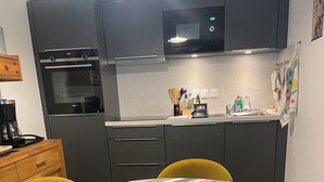 Une cuisine moderne équipée d’un four à micro-ondes, d’un four et d’un évier. On y trouve une table à manger recouverte d’une nappe à rayures et entourée de chaises jaunes.