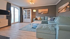 A modern living room with a sofa, a coffee table, a cabinet, and a flat-screen TV. - Vacation apartment Wellenreiter (Norderney)