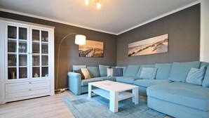 A living room with a light blue sofa, a white coffee table, and a cabinet with glass doors. - Vacation apartment Wellenreiter (Norderney)