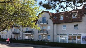 A row of multi-story buildings with balconies, a paved sidewalk, and a cyclist. - Vacation apartment Wellenreiter (Norderney)