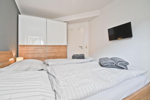 A hotel room with a bed, a wardrobe, a flat-screen TV, and a door.