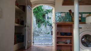 An interior view of a home with a stone staircase leading to an outdoor area, a bookshelf, and a washing machine. - Pied-à-terre de Saint-Paul | Free public parking (Saint-Paul-de-Vence)
