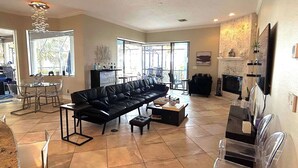 A spacious living room with a black leather sofa, a glass dining table, and a fireplace. - Florida Space Coast Waterfront Retreat - Family & Pet Friendly - Sleeps up to 15 (Cocoa)