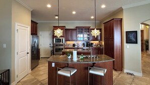 A modern kitchen with granite countertops, stainless steel appliances, and wooden cabinets. There are two pendant lights with star-shaped shades and a large island with bar stools. - Florida Space Coast Waterfront Retreat - Family & Pet Friendly - Sleeps up to 15 (Cocoa)