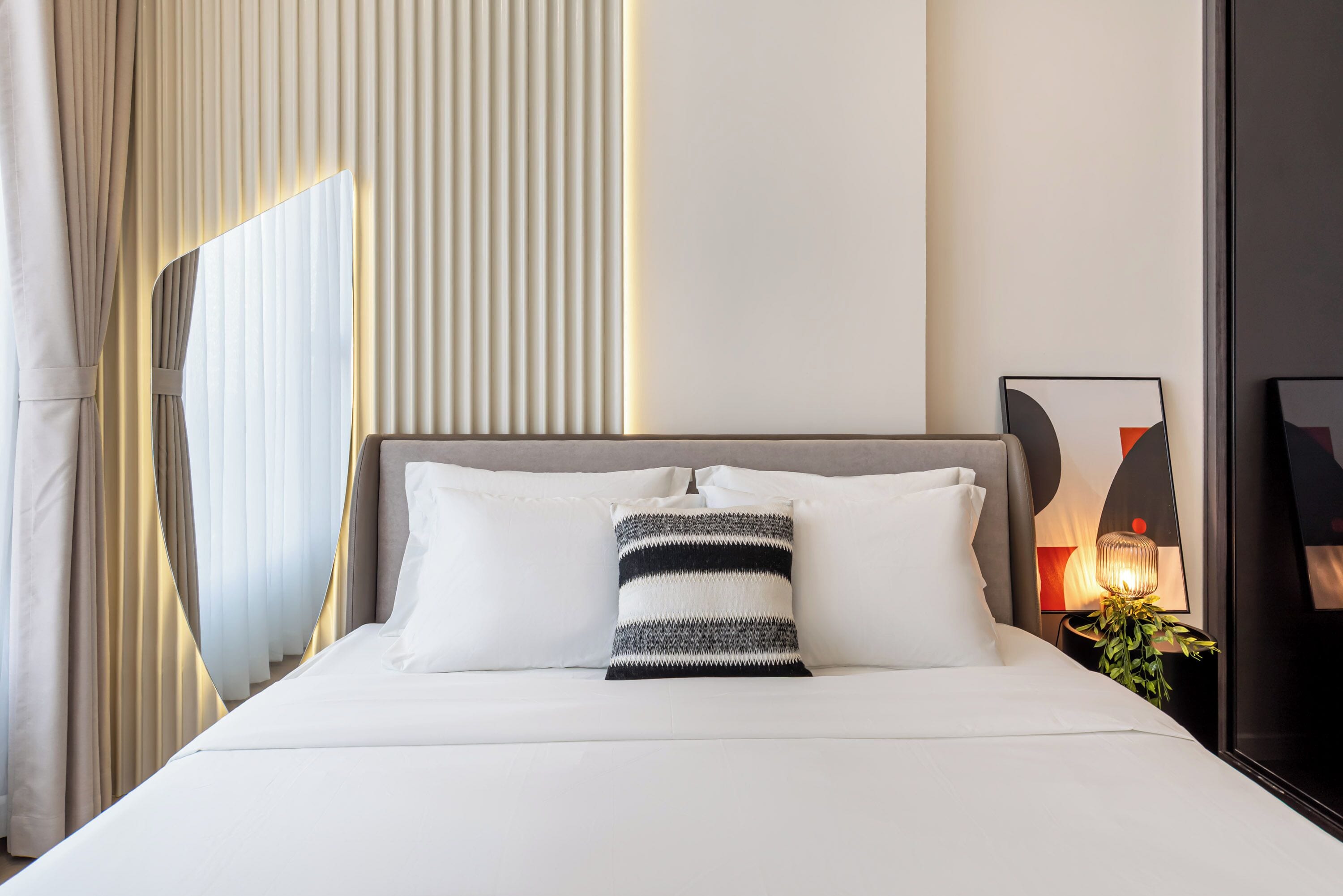 A neatly made bed with white linens and a striped pillow, a bedside table with a lamp, and a framed picture on the wall.