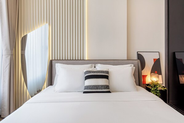 A neatly made bed with white linens and a striped pillow, a bedside table with a lamp, and a framed picture on the wall.