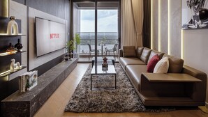 Uma sala de estar moderna com uma TV grande exibindo 'NETFLIX', um sofá de couro, uma mesa de centro e vista da cidade através de grandes janelas.