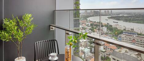 A balcony with a table and chairs, a potted plant, and a view of a cityscape and river.