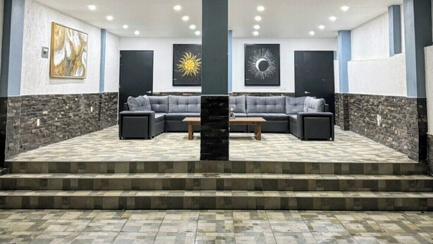 A covered outdoor seating area with a sofa and a coffee table, a staircase leading to an upper level, and three framed artworks on the wall.