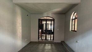 A hallway with a tiled floor, a large arched doorway, and a small window on the right wall.