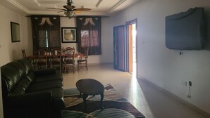 Un soggiorno con un divano in pelle nera, un tavolo da pranzo con sedie, un lampadario e un'ampia finestra con tende.