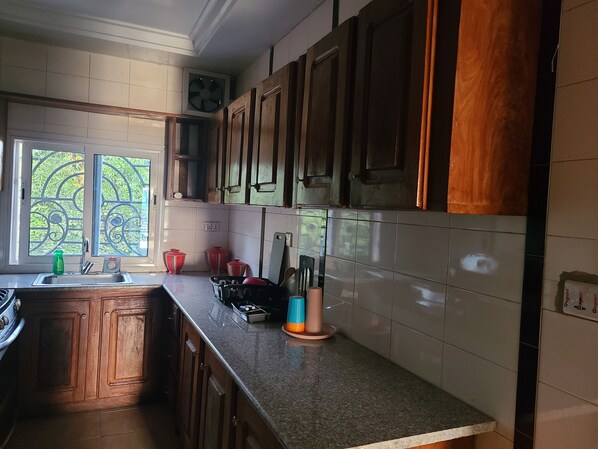 A kitchen with wooden cabinets, a granite countertop, and a window with a view of greenery.