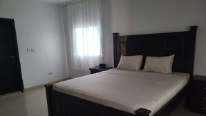Un letto ben rifatto con testiera in legno, un comodino e una finestra con tende leggere.
