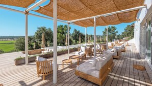 An outdoor deck with wooden furniture, a large woven canopy, and a view of the landscape. - Quinta Amala (Grandola)