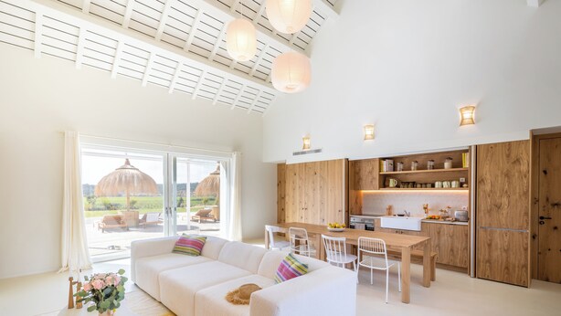 A modern interior with a white sofa, dining table, and chairs, wooden cabinets, and a large window with a view. - Quinta Amala (Grandola)