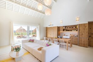 A modern interior with a white sofa, dining table, and chairs, wooden cabinets, and a large window with a view.