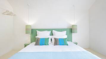 Una cama con ropa de cama blanca y azul, dos almohadas con diseños a rayas y lisos, y lámparas verdes fijadas a la pared.