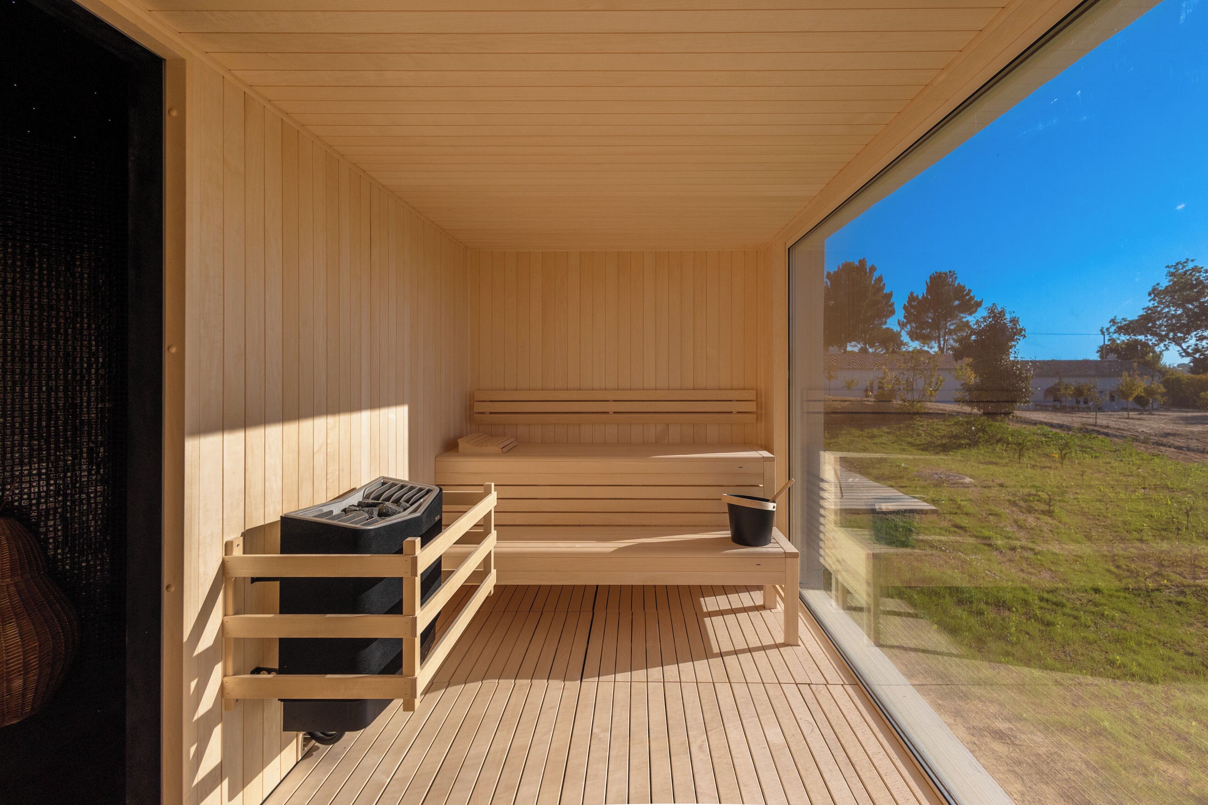 A sauna room with wooden benches and a glass door leading to a grassy area.