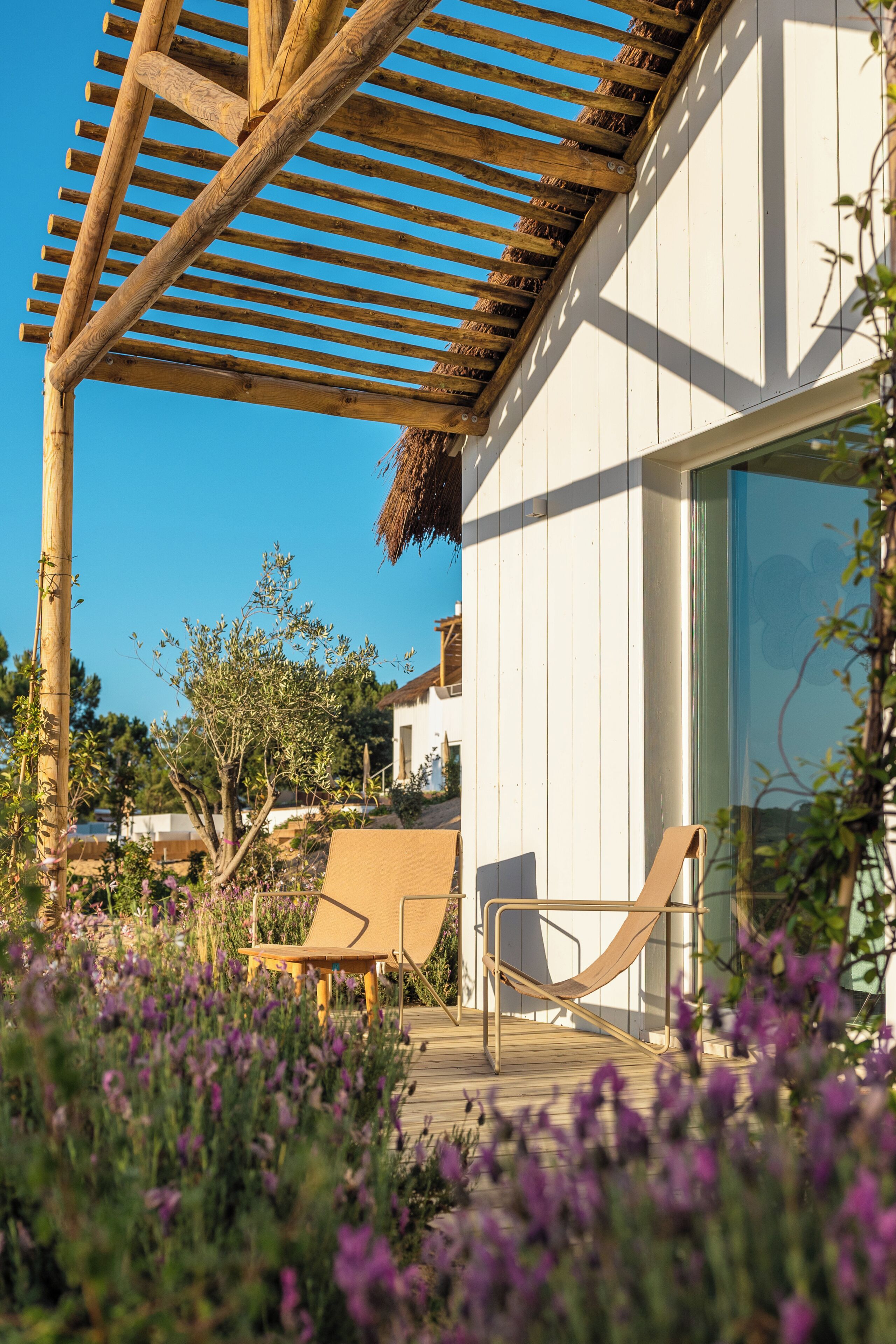 A wooden pergola, a white building, and a deck with two chairs.