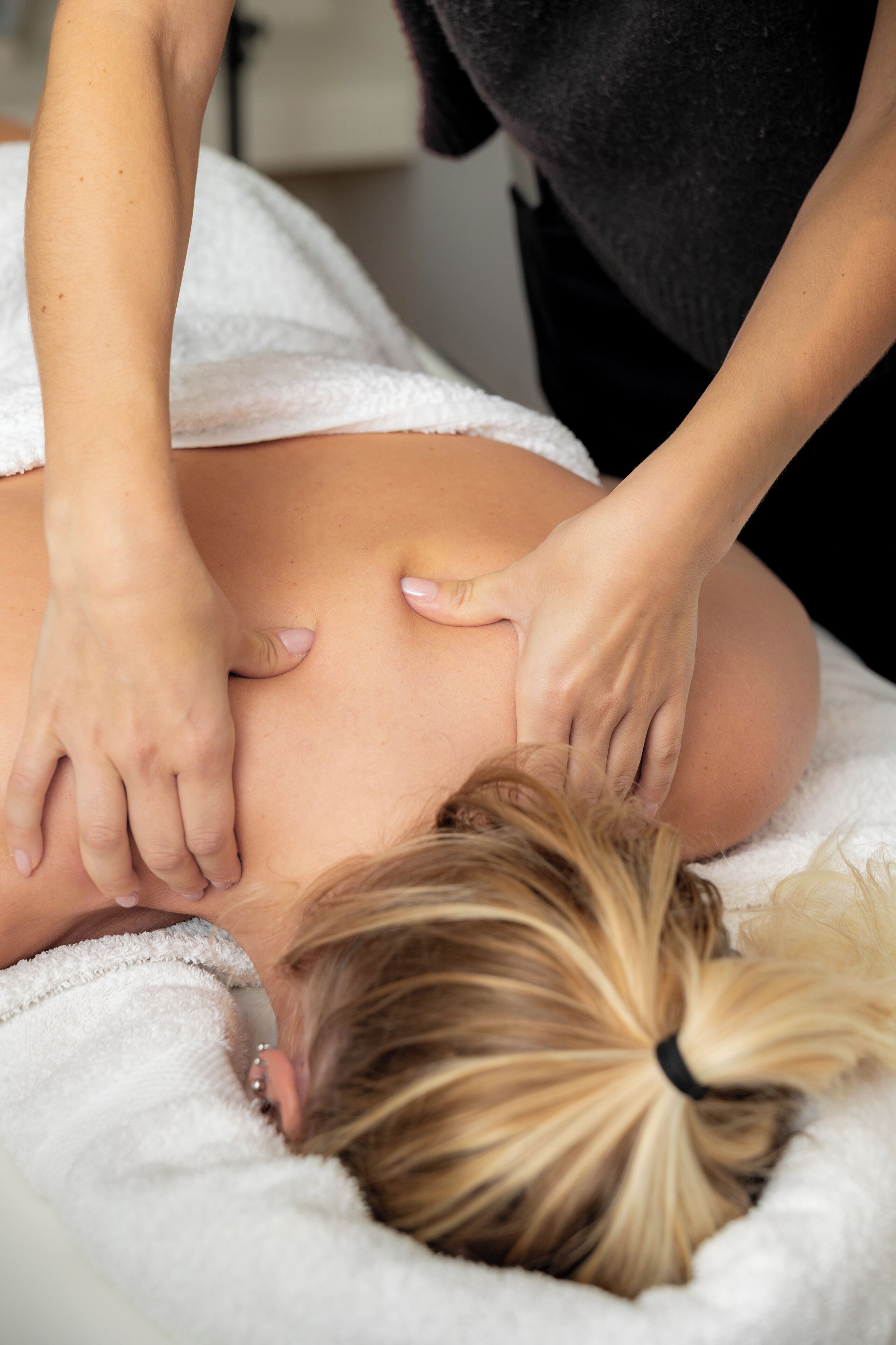 Eine Person erhält eine Massage auf einem mit einem weißen Handtuch bezogenen Bett.