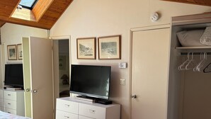 Ein Schlafzimmer mit schrägem Dach, einem Fernseher auf einer Kommode, einem Kleiderschrank und zwei Betten mit floralem Bettbezug.