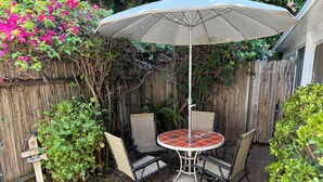 Eine Terrasse mit einem runden Tisch, Stühlen, einem Sonnenschirm und einem Holzzaun.