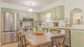 A kitchen with green cabinets, stainless steel appliances, and a wooden dining table.