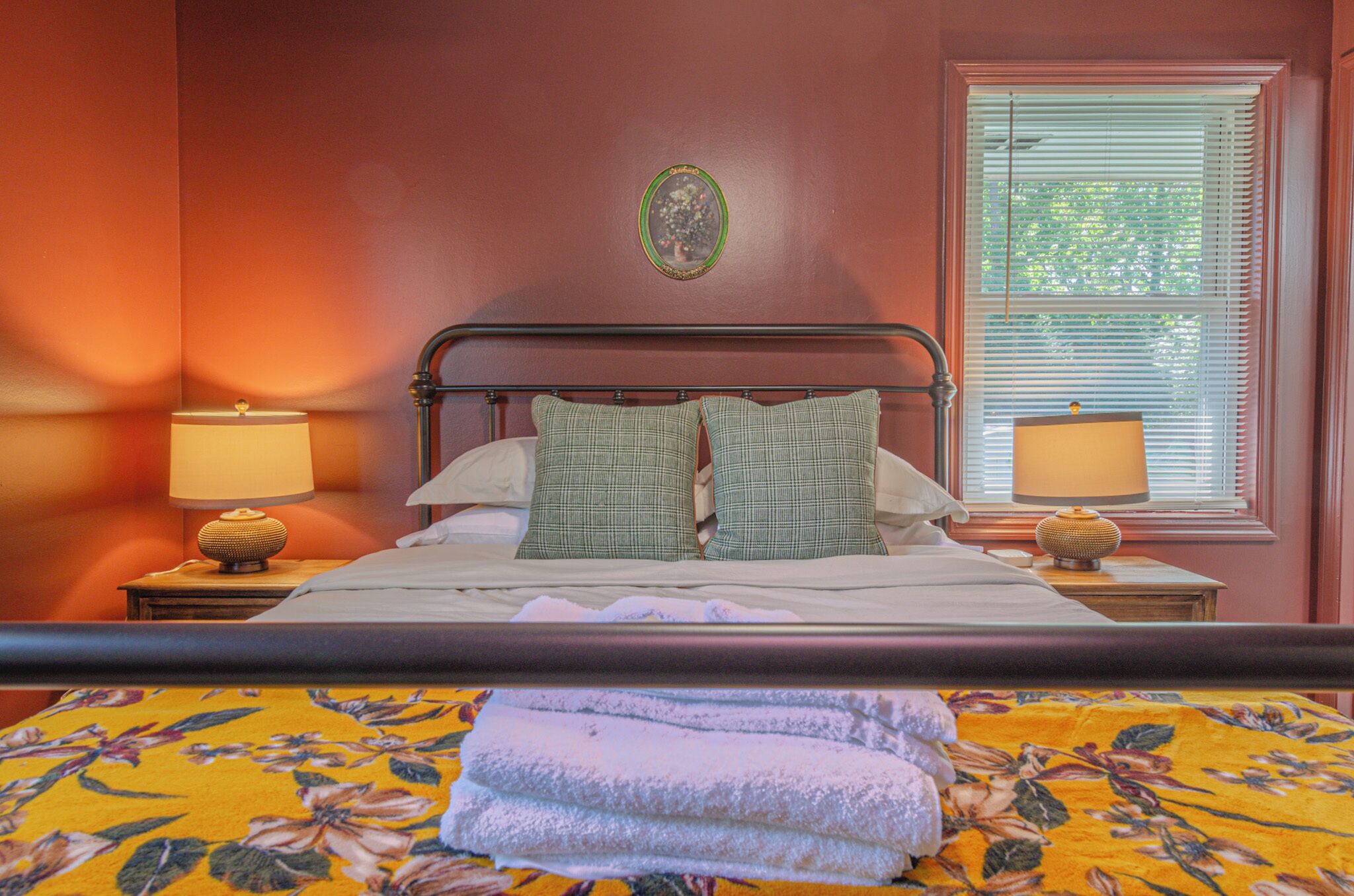 Una cama con cubrecama floral, dos almohadas verdes y dos lámparas de noche sobre mesitas de madera.