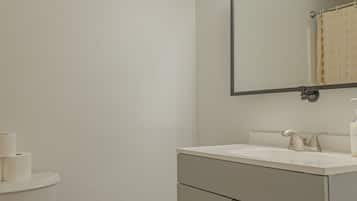 Un baño con inodoro, lavamanos, espejo y un cubo de basura.