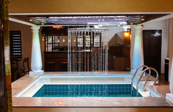 Une piscine agrémentée d’une cascade, entourée d’un bar avec des tabourets et d’un espace salon.
