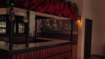 Un espace bar avec un comptoir en bois, des luminaires suspendus et des décorations florales rouges.