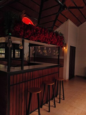 Un espace bar avec un comptoir en bois, des luminaires suspendus et des décorations florales rouges.
