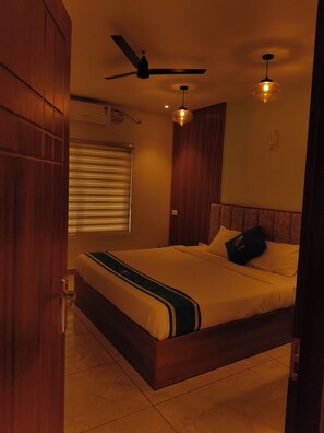 Une chambre à coucher comprenant un lit, un ventilateur de plafond, une fenêtre avec des stores et un luminaire fixé au mur.