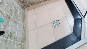 A bathroom with a tiled floor, a drain, and a black edge along the wall.