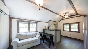 A spacious room with a wooden ceiling, a sofa, a small table, and a kitchen area with a refrigerator. - Tiny House w/Creek and Eagles (Millersburg)