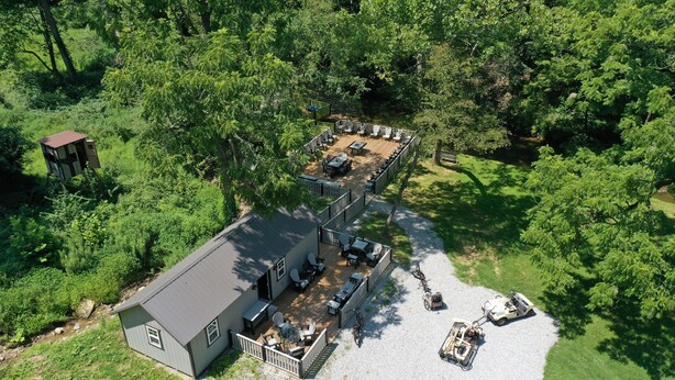 A two-story cabin with a deck, surrounded by dense forest. - Tiny House w/Creek and Eagles (Millersburg)