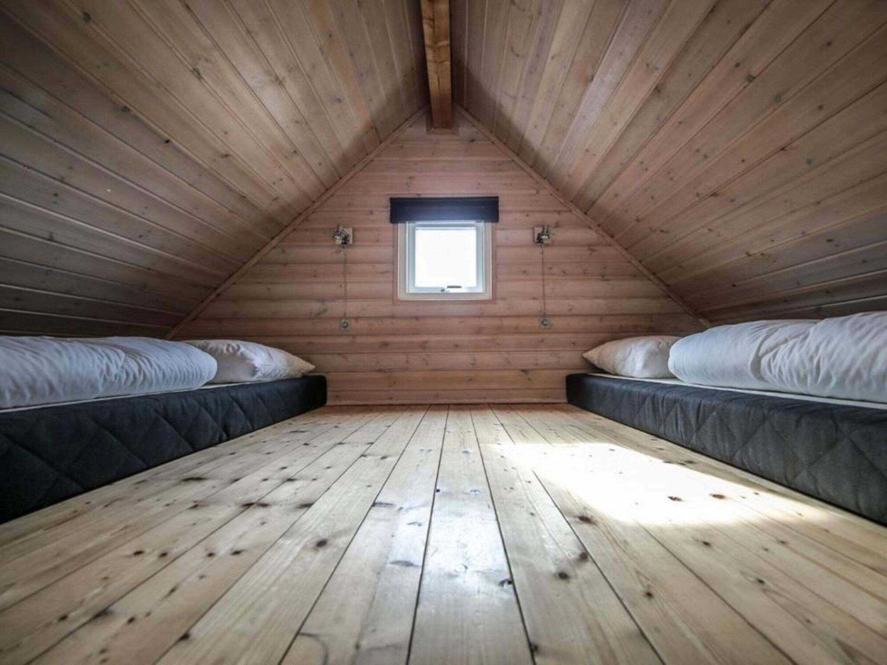 Una piccola camera da letto in mansarda, con pareti in legno e soffitto a spiovente. Sono presenti due letti con materassi e cuscini. Una piccola finestra fa entrare luce naturale nella stanza.