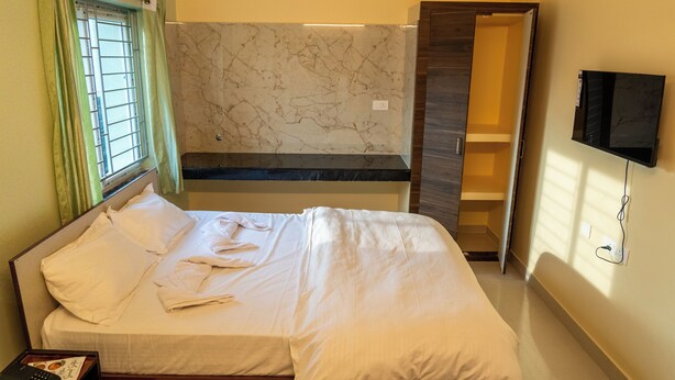 A hotel room with a bed, a TV, a bathroom, and a marble wall. - Nivas Stays (Bhubaneshwar)