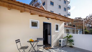 A balcony with a table and chairs, a potted plant, and a building in the background. - Olga Apt 4- Lovely Studio on Ground Floor (Limassol)
