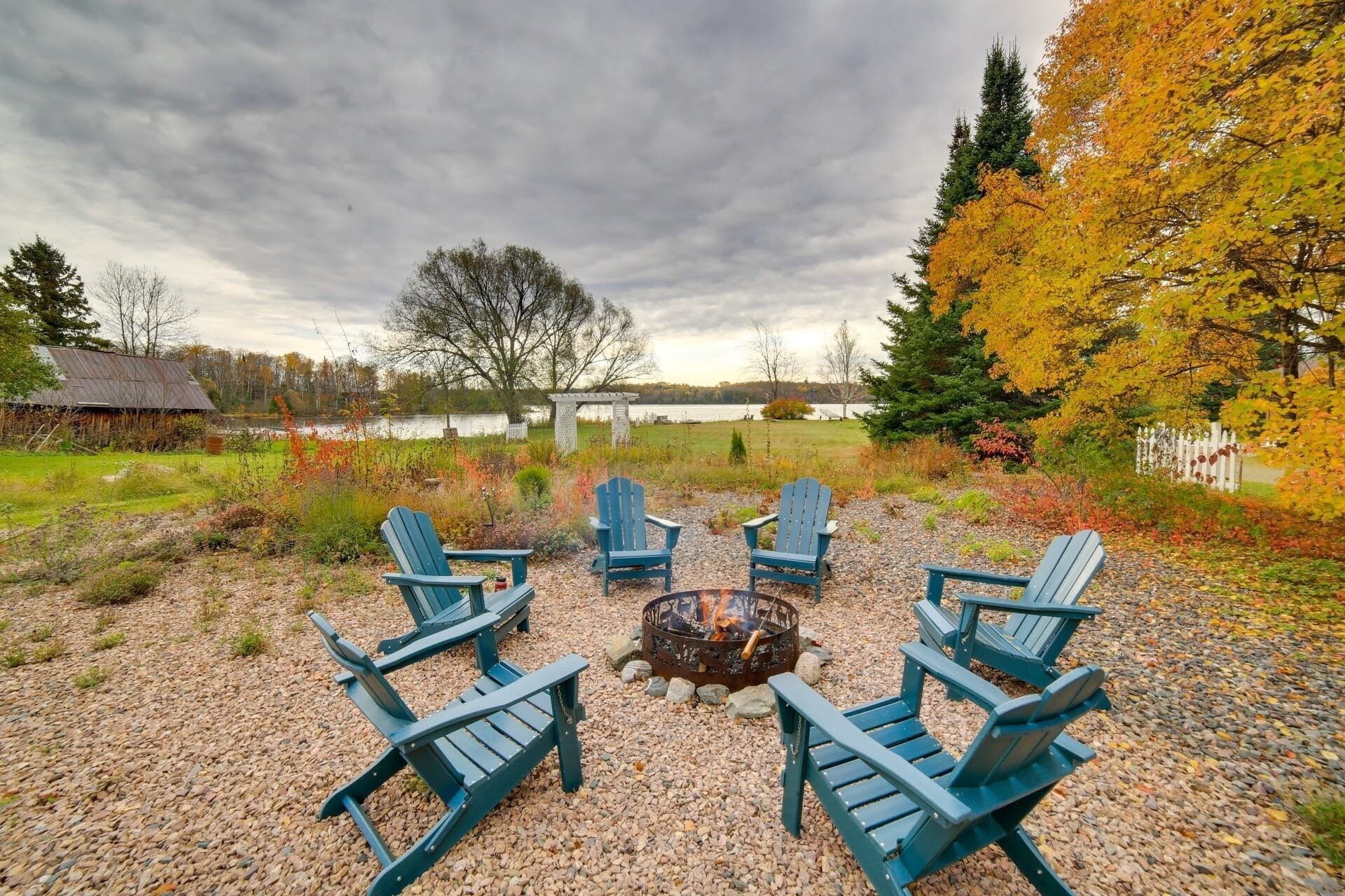 A gravel patio with four Adirondack chairs arranged around a fire pit.