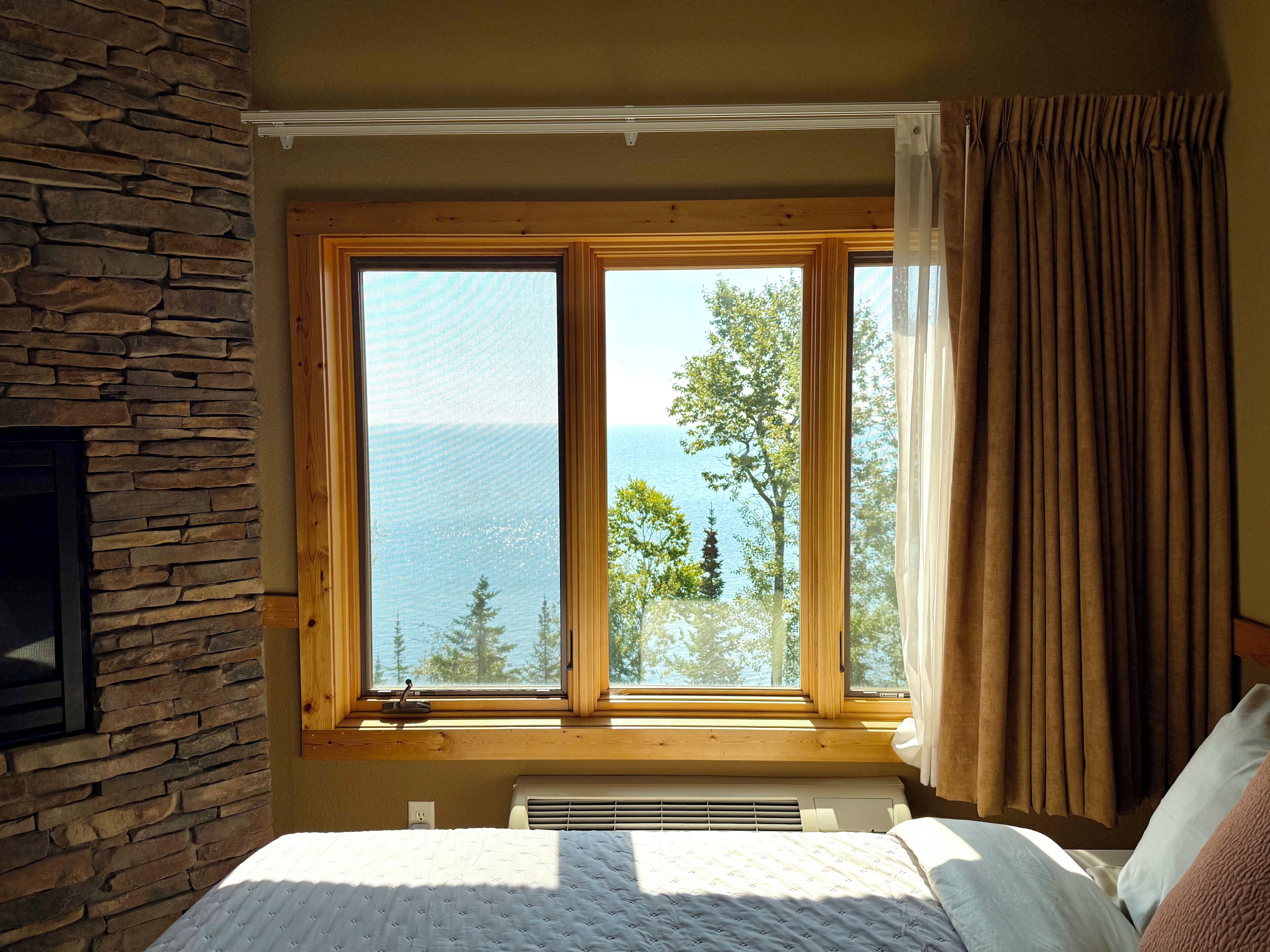 A bedroom with a large window, stone wall, and a bed with white bedding.