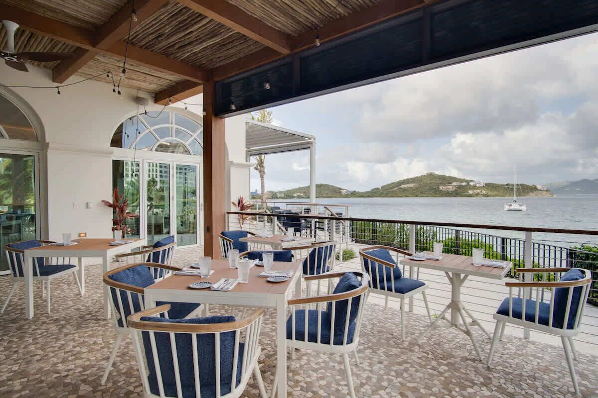 Une terrasse avec des tables et des chaises, donnant sur une étendue d’eau et une île lointaine.