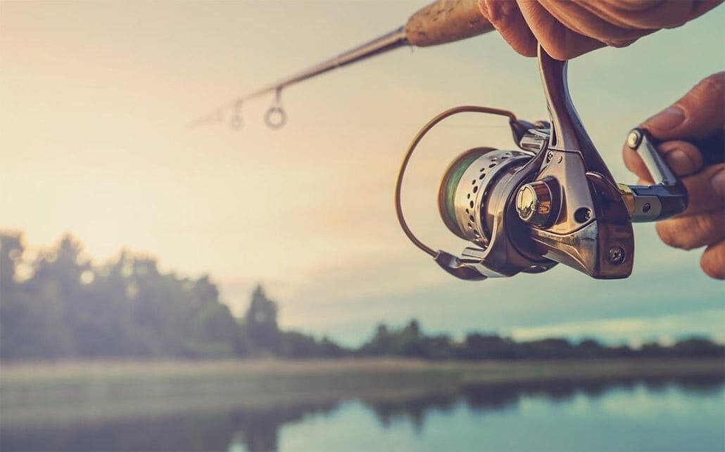 A close-up of a fishing rod with a reel, held by a hand.