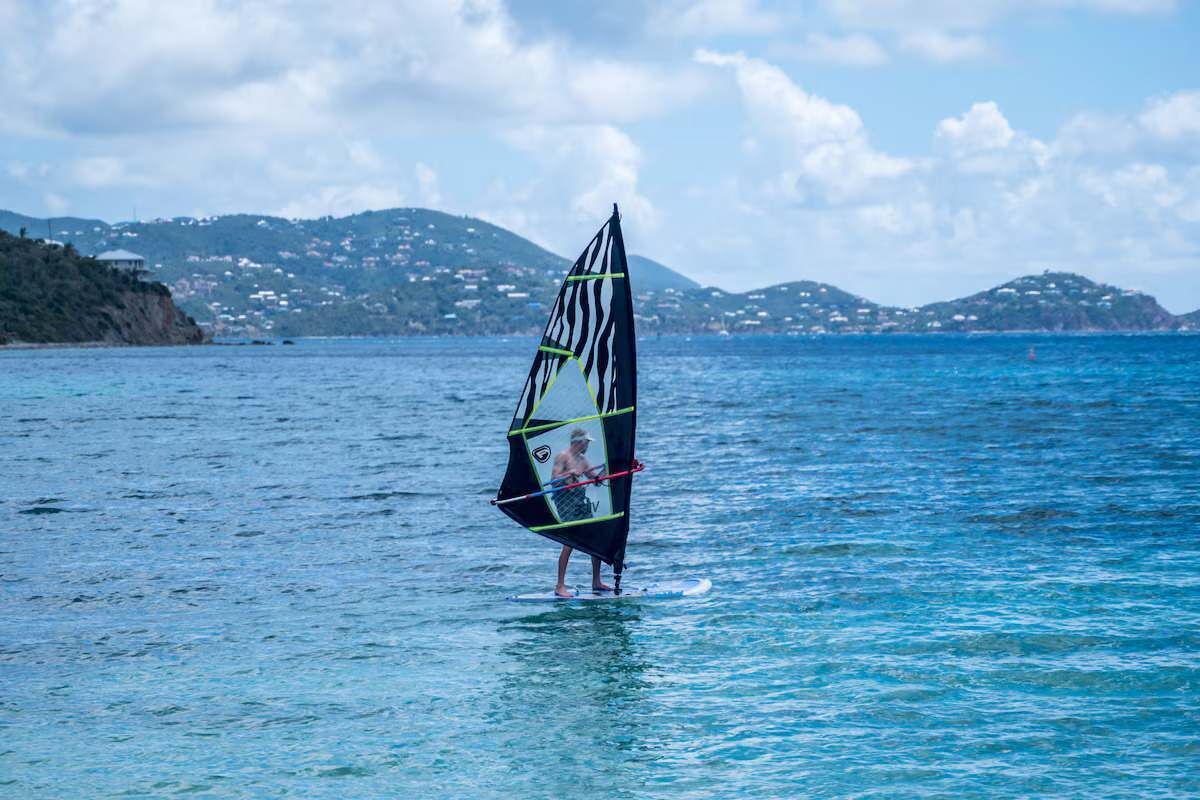 Iemand windsurft op het water, met een bergachtig landschap op de achtergrond.