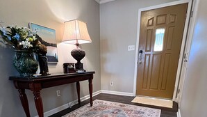 Un couloir avec un tapis à motifs, une console sur laquelle est posée une lampe, et une porte dotée d’une fenêtre.