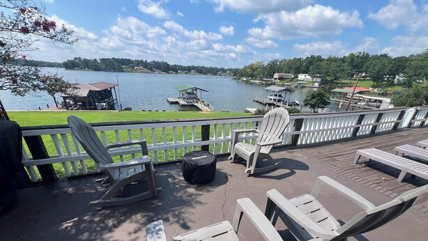 Une terrasse dotée de chaises Adirondack, d’un espace salon couvert et offrant une vue sur un lac, avec des bateaux et des maisons en arrière-plan.