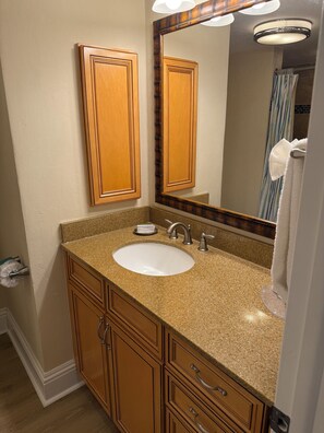 Baño con lavamanos de encimera de granito, armarios de madera, un espejo y un perchero para toallas.