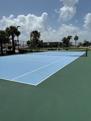 Una cancha de tenis con una red, rodeada de palmeras y edificios.